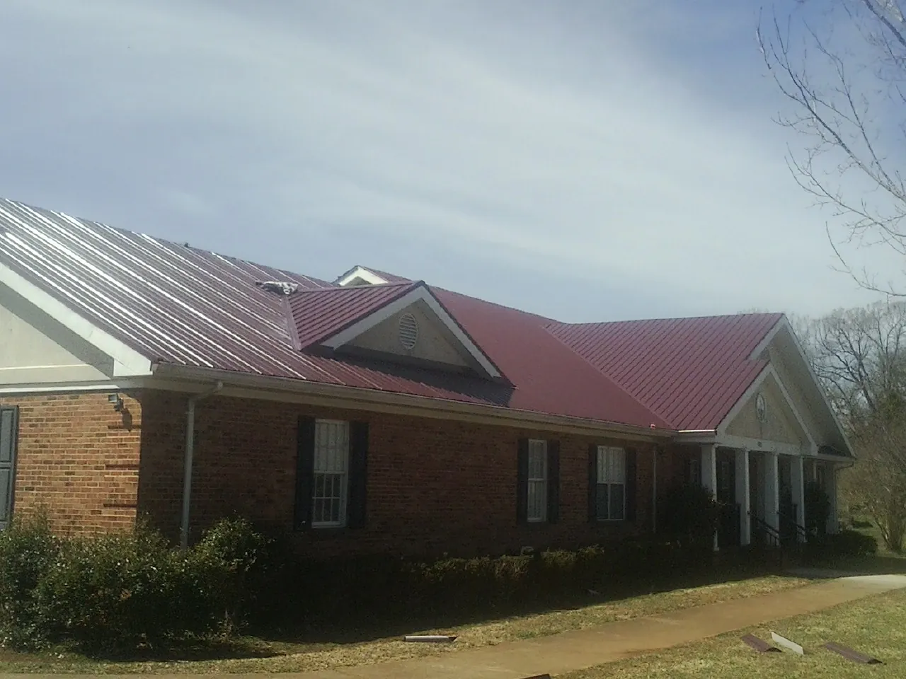 Red metal roof with gabled entries on a long brick building, from a Hail Damage Roof Repair job in Putney