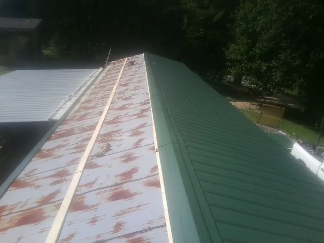 Old rusted panels beside newly installed green metal roofing — Wind Damage Roof Repair by Roofing Brothers in Putney