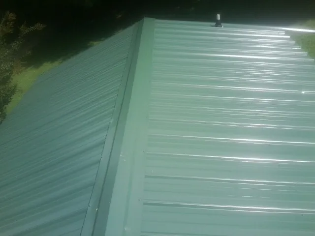 New green metal panels meeting at the ridge of a roof — Flat Roof Repair work by our crew in Putney