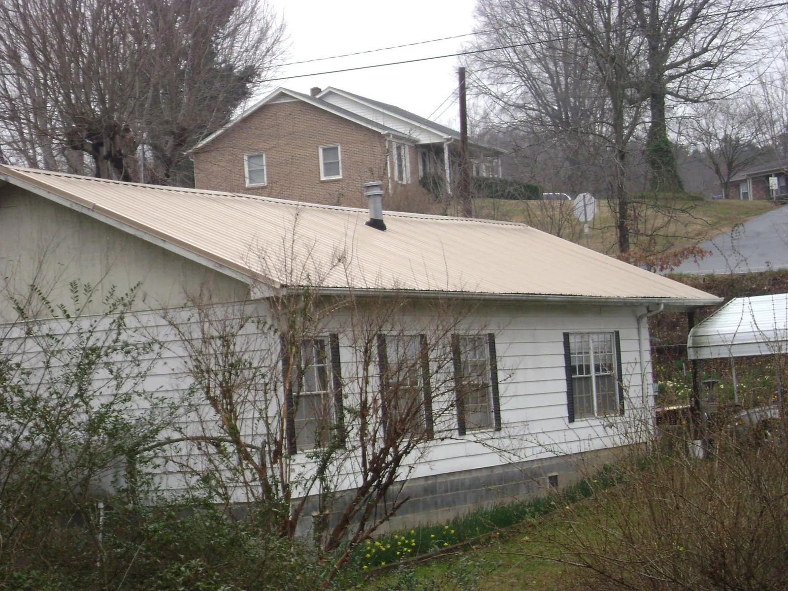 Tan metal roof on a white sided house set into a hillside — Commercial Roofing by Roofing Brothers in Putney